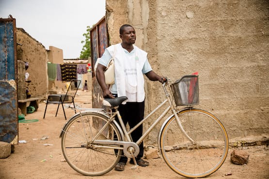 Malaria Consortium community health worker standing behind a bike