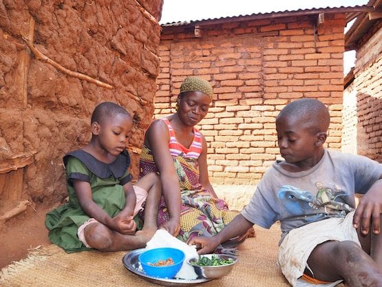 Mother and two kids on mat eating ugali