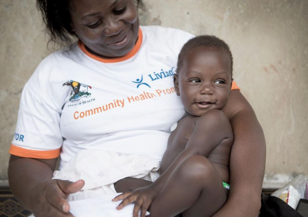 A woman in a white Living Goods t-shirt smiling down at the baby sitting in her lap.