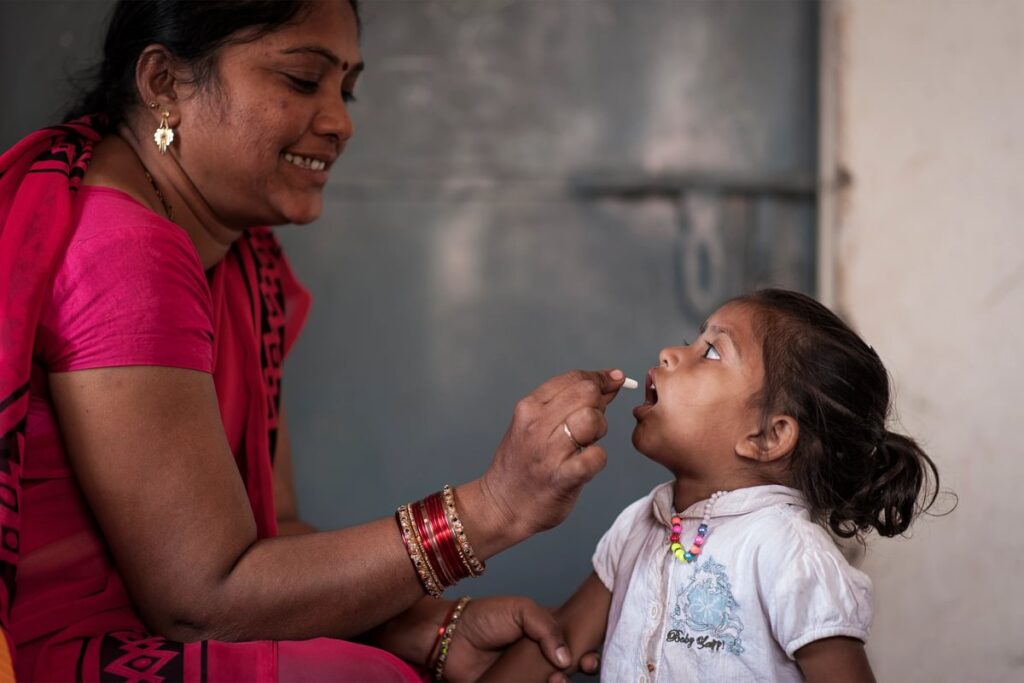 A women giving a young girl medicine, Evidence Action match campaign